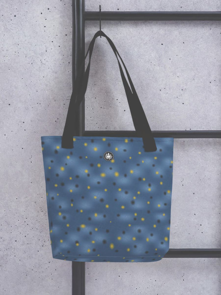 Tote bag with black straps and blue body in painted infurcata design hanging on black ladder in front of a grey concrete wall.