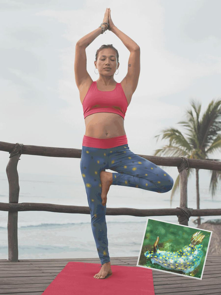 Woman in tree yoga pose on red mat wearing painted infurcata yoga leggings with the ocean in the background. 