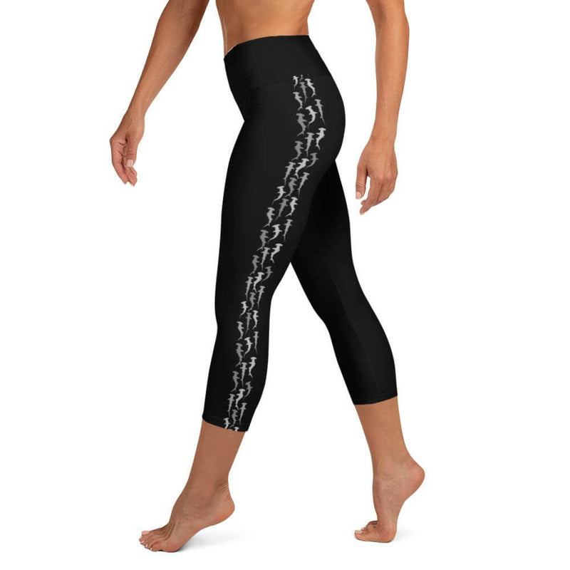 A person wearing casual capri length yoga leggings in black with hammerhead shark pattern on the outside of each leg.