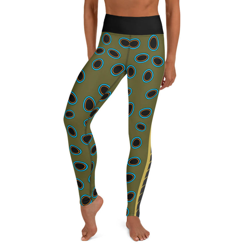 A person wearing olive green yoga leggings in a spotted mandarin inspired pattern of black ovals outlined in turquoise, gold.